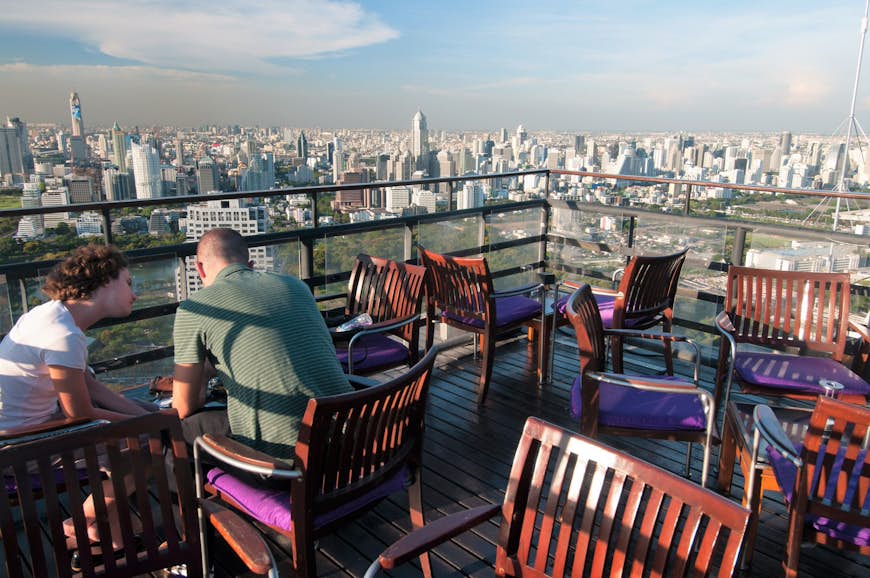 Daytime view of Moon Bar rooftop, people sit at a table with the sprawling cityscape in the background © Austin Bush / Lonely Planet
