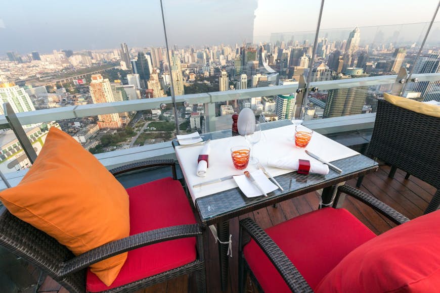View of a table and two chairs at the edge of Red Sky rooftop bar, with a clear view of the city below © Stephane Bidouze / Shutterstock