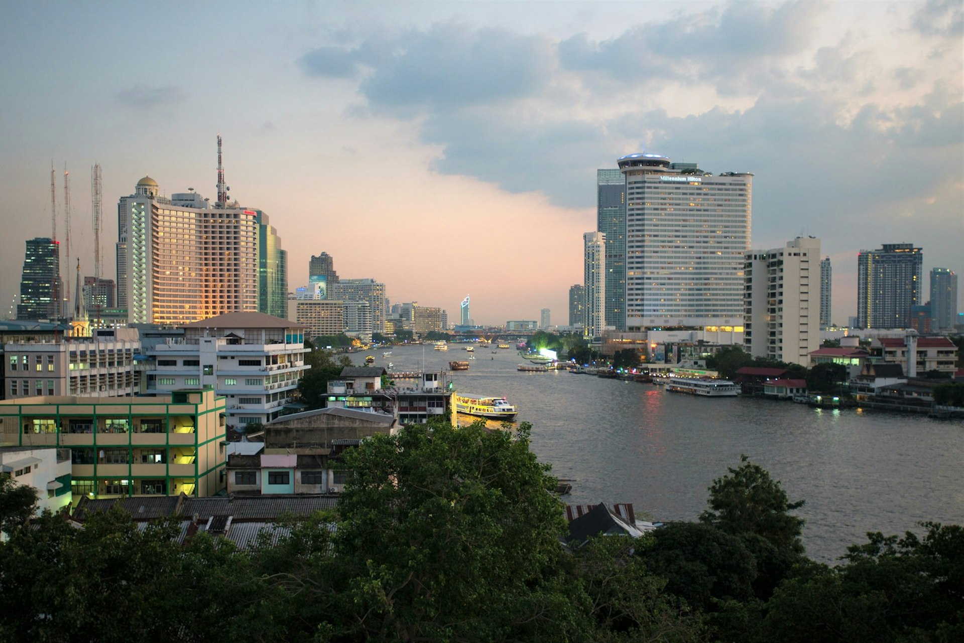 High view of Chao Praya River at dusk, lined with tall city buildings © Austin Bush / Lonely Planet
