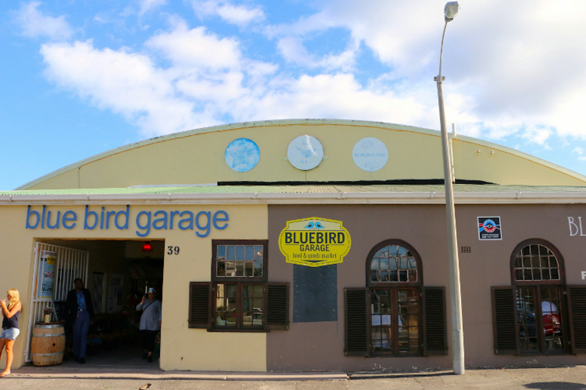 A faded yellow hanger-looking building with curved roof has a large blue sign reading 'blue bird garage'.
