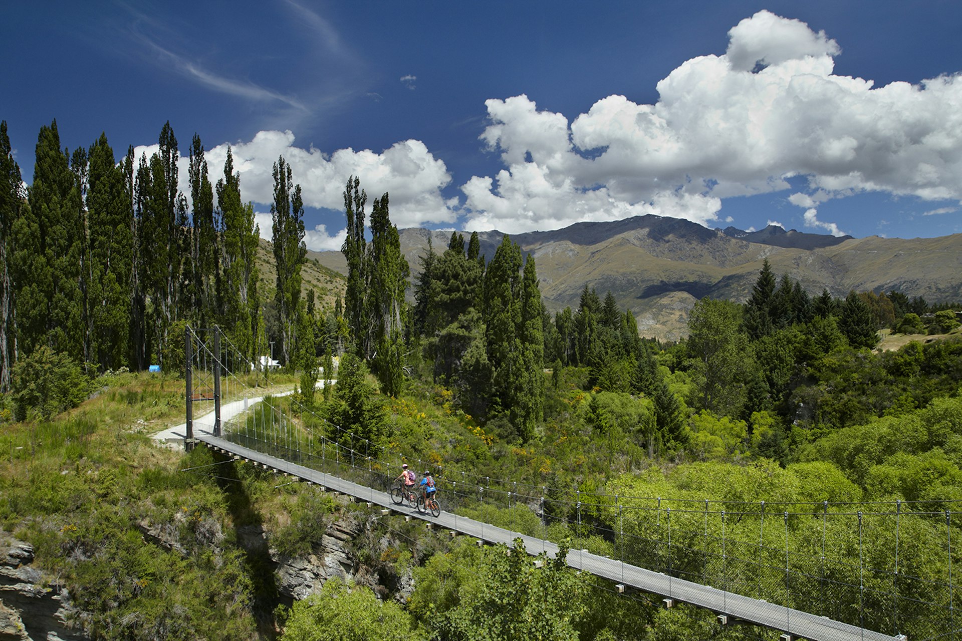 Cyclists crossing a suspension bridge on New Zealand's Arrow River Bridges Trail. Image by Danita Delimont / Gallo Images / Getty Images