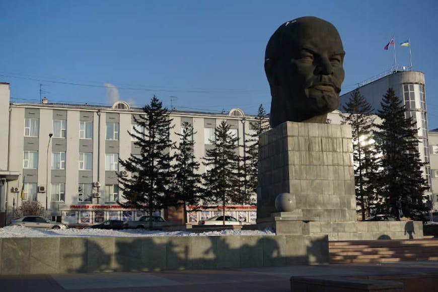 Ett enormt Leninhuvud av svart sten står på en sockel i snön utanför en station