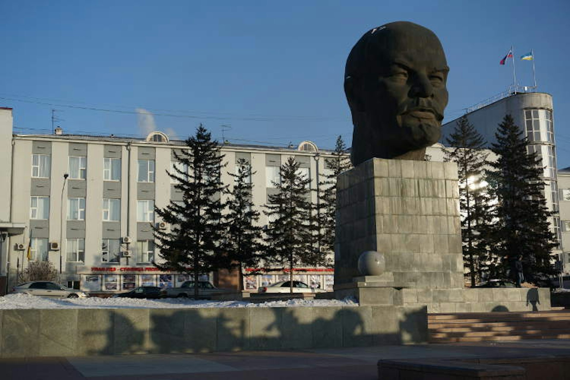 An enormous head of Lenin made of black stone stands on a plinth in the snow outside a station