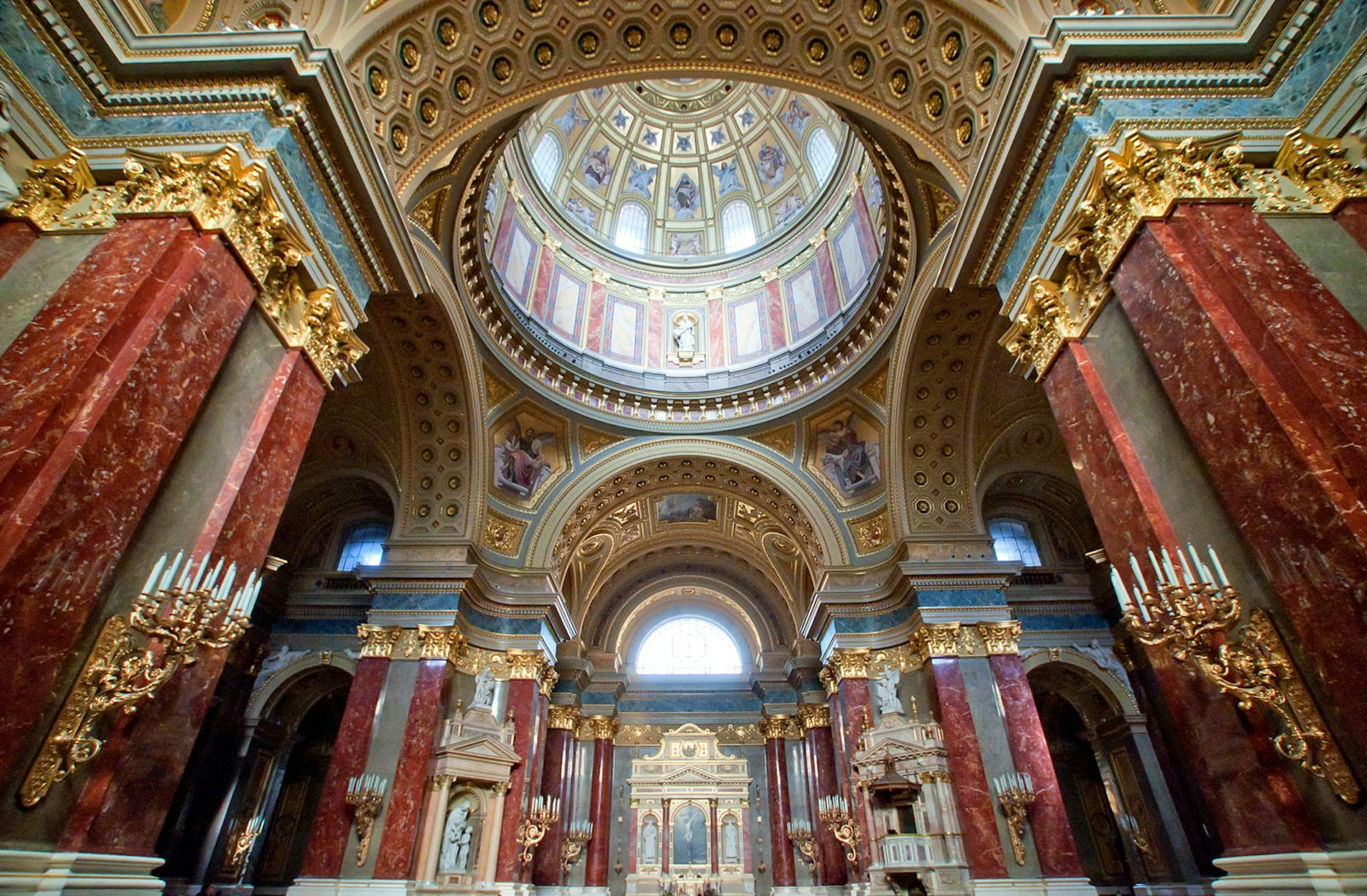 The ornate interior of the Basilica of St. Stephen, with red walls, a large dome and gold altar