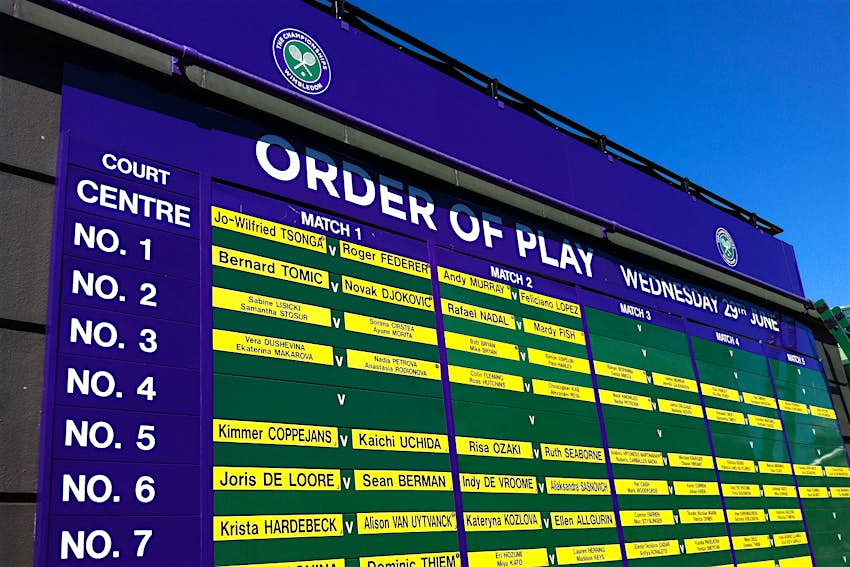 Features - Order_of_play Under a blue sky sits a large purple-and-green billboard which notes (with bright yellow labels with black lettering) what are the first, second, third, fourth and fifth matches (noting each competitors name) on each of the courts at Wimbledon on the day