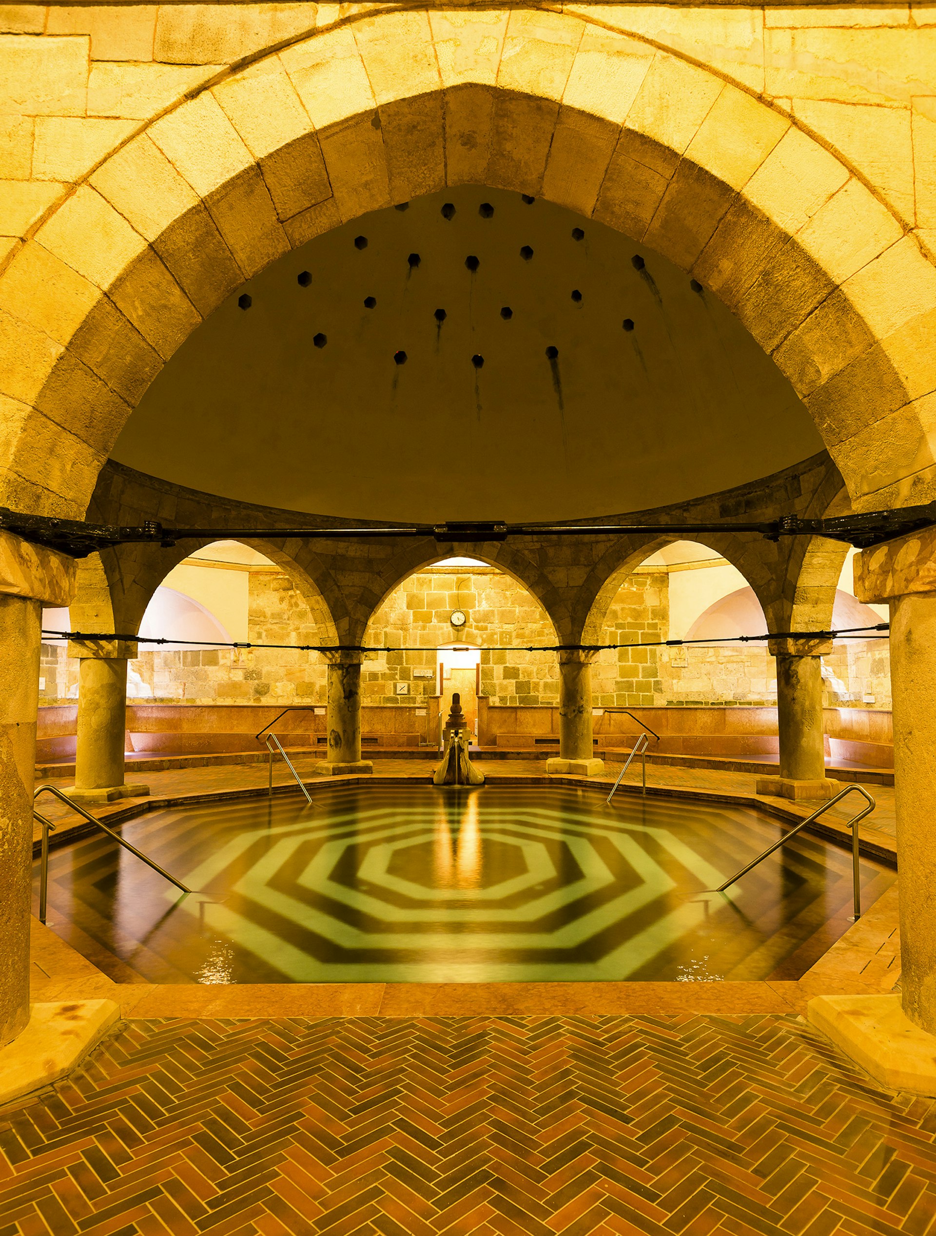 An octagonal pool sits below a domed ceiling in the warmly lit Rudas Baths, Budapest, Hungary