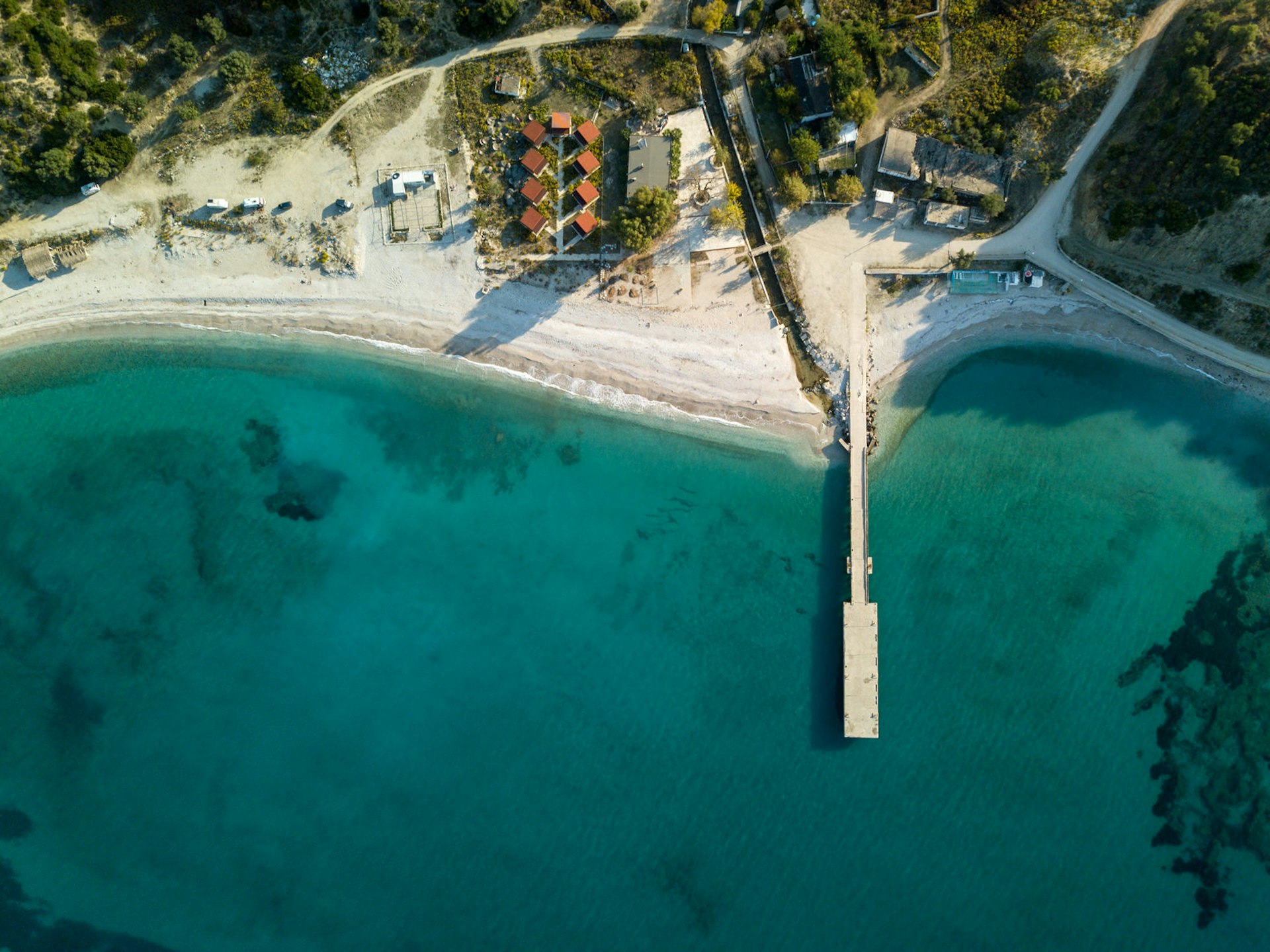 A drone shot of Bunec beach from above with a white strip of sand and wooden pier jutting out into the sea
