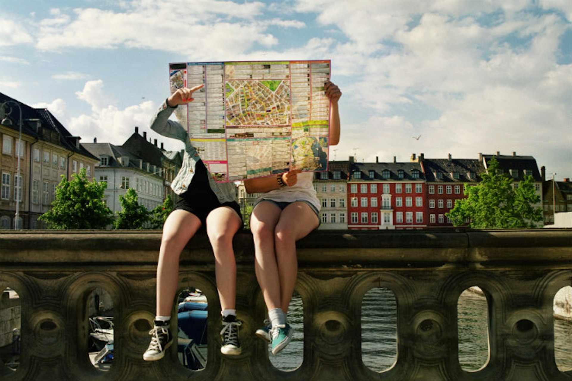 Two teenage girls sitting on bridge holding city map in front of them. Copenhagen city centre.