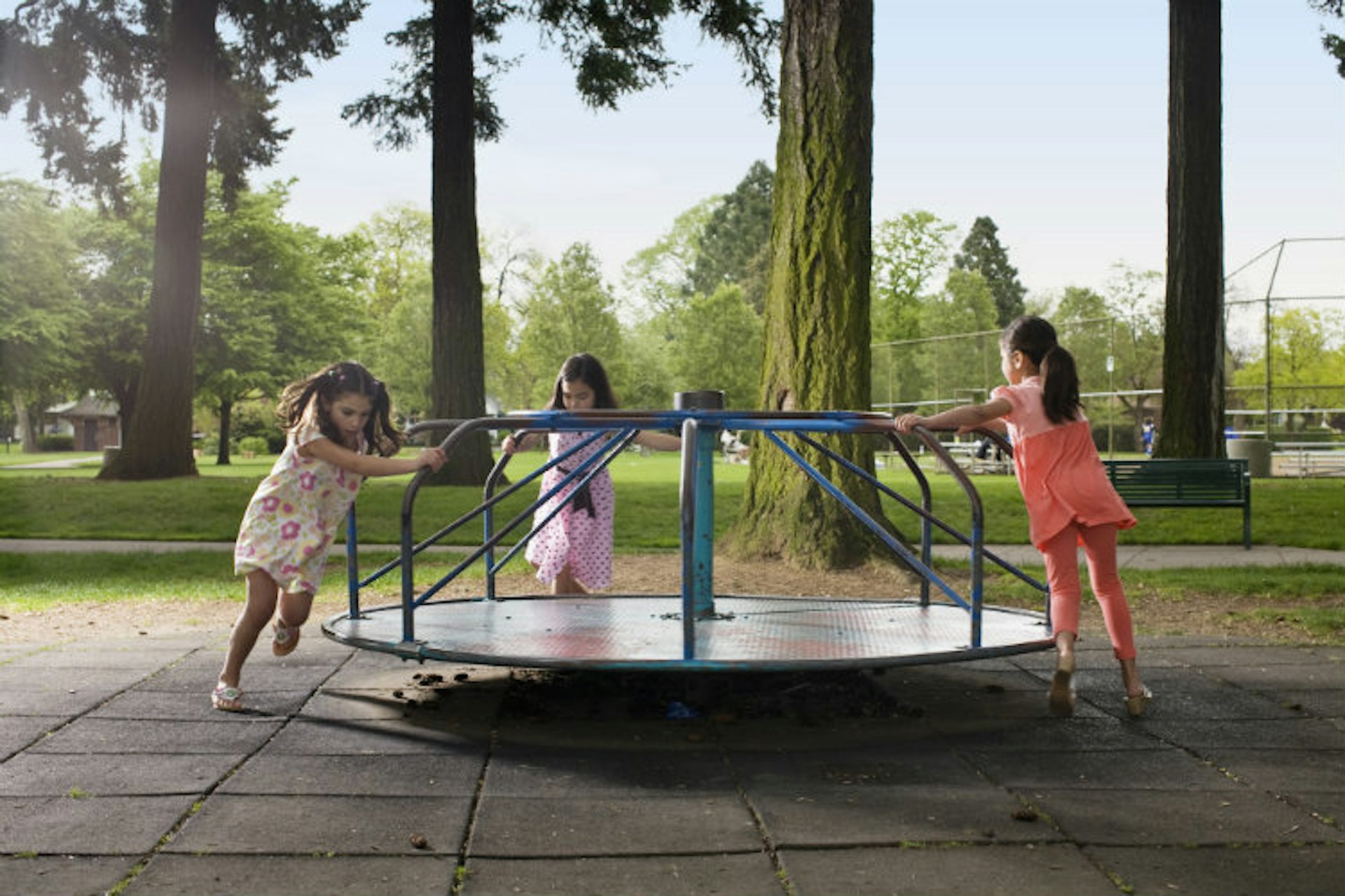 Three girls pushing roundabout in playground