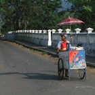 Features - A food vendor pushes his food cart along a sleepy street in the Spice Islands. Image by Peter Charlesworth