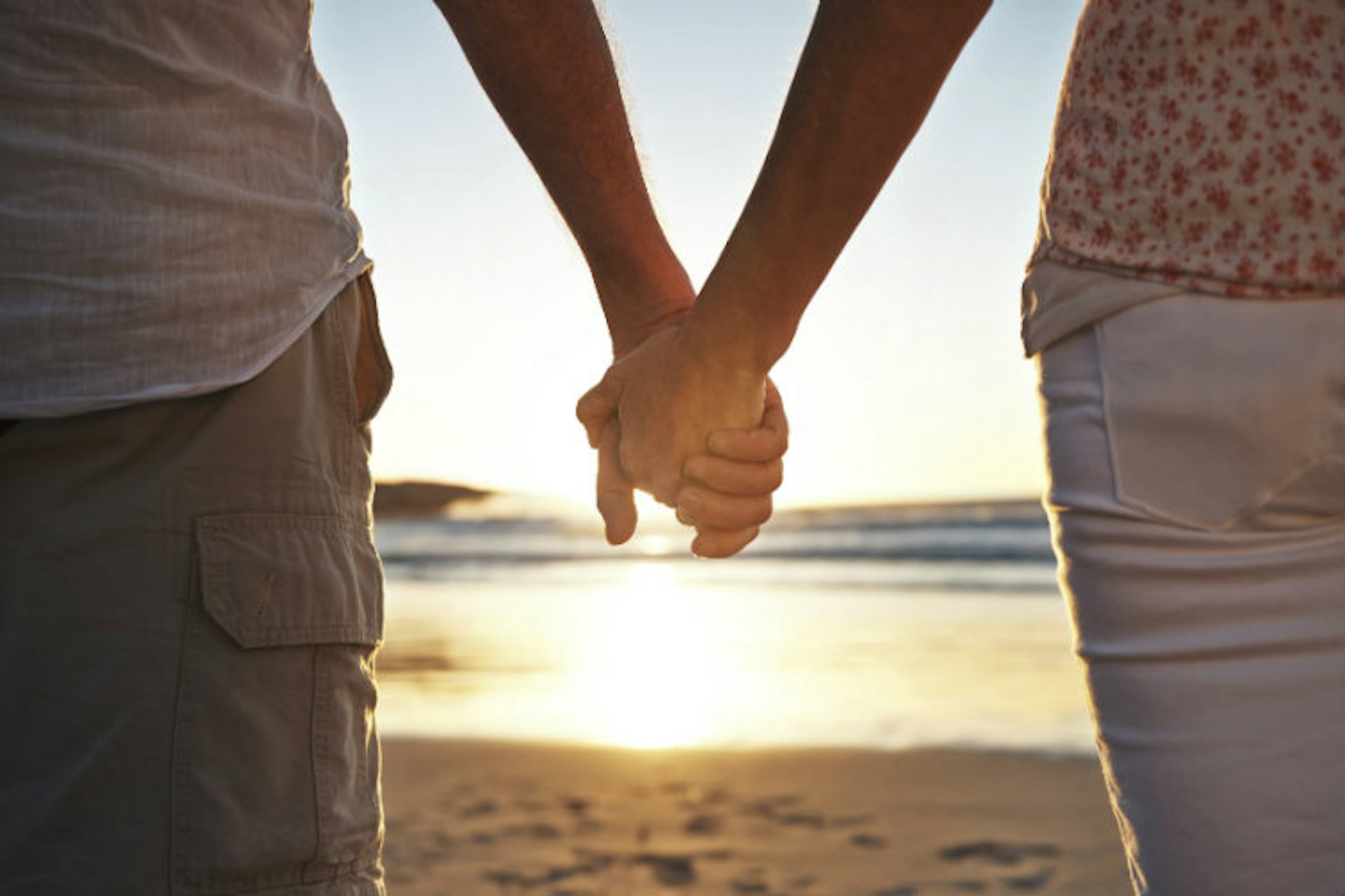 A couple hold hands on a beach as the sun sets.