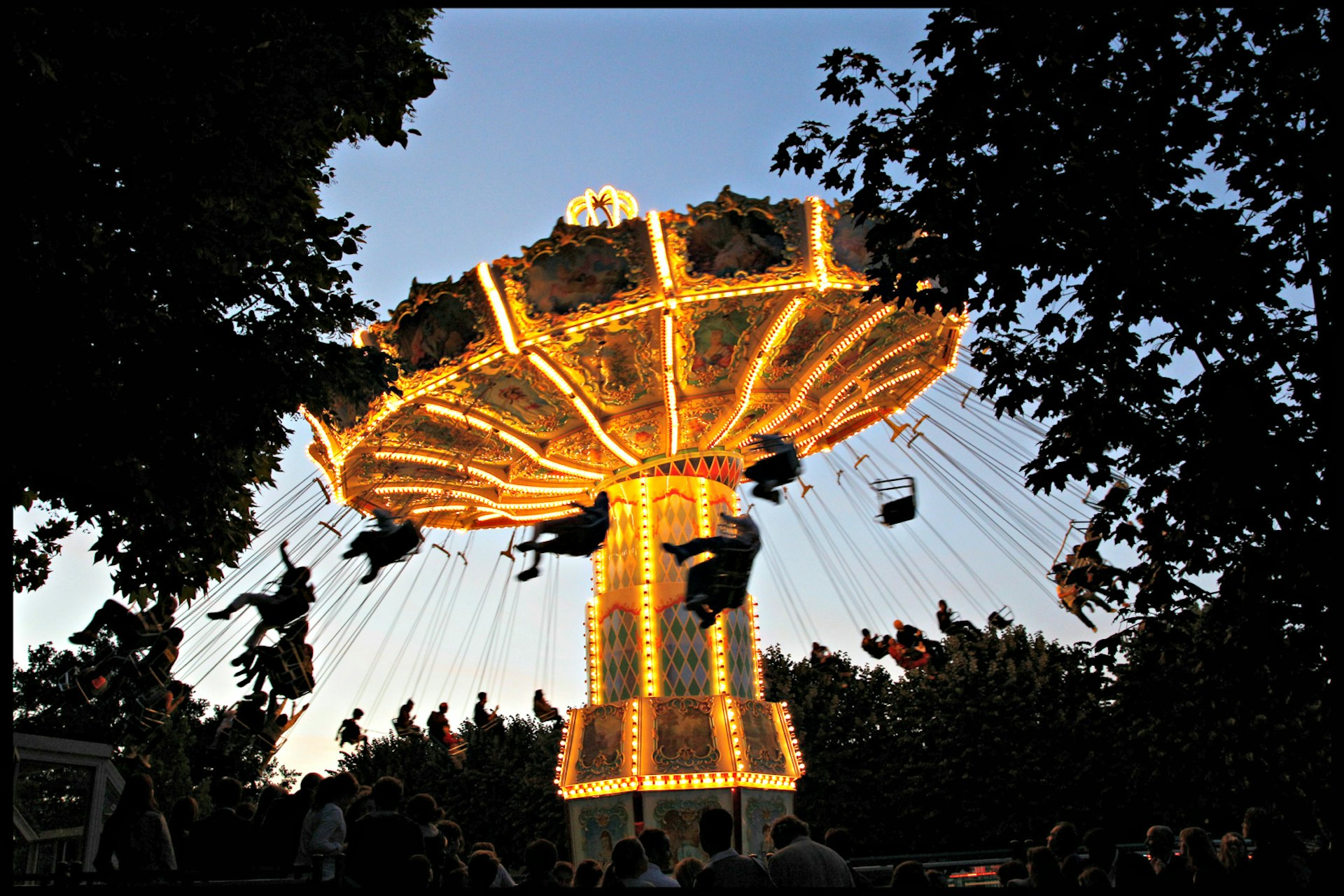 Swing ride carousel all lit up at dusk, with riders silhouetted at Jardin D'Acclimatation in Paris