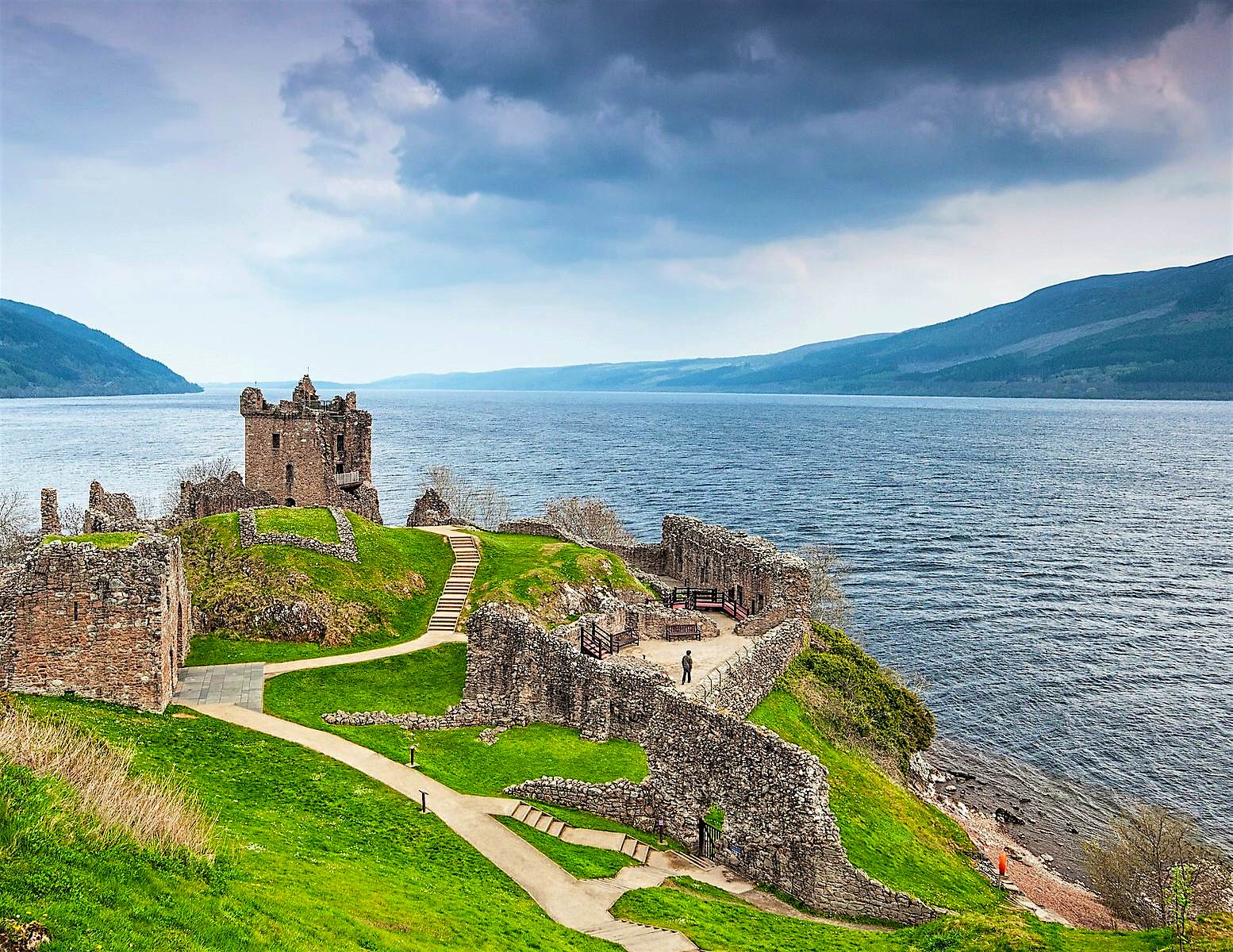 Features - shutterstockRF_405276580-252b34000420 A castle on a green outcropping with a long winding road overlooking the dark blue expanse of Loch Ness
