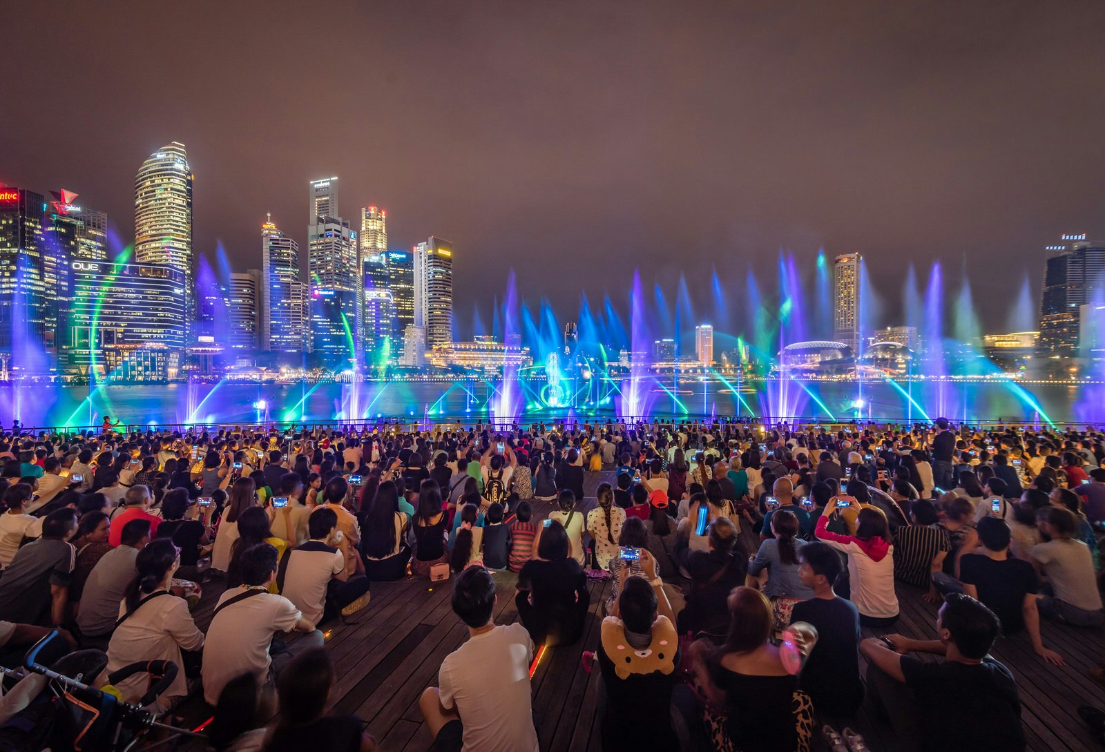 A crowd of people watch a colourful light show with the Singapore skyline backdrop © maison photography / Shutterstock