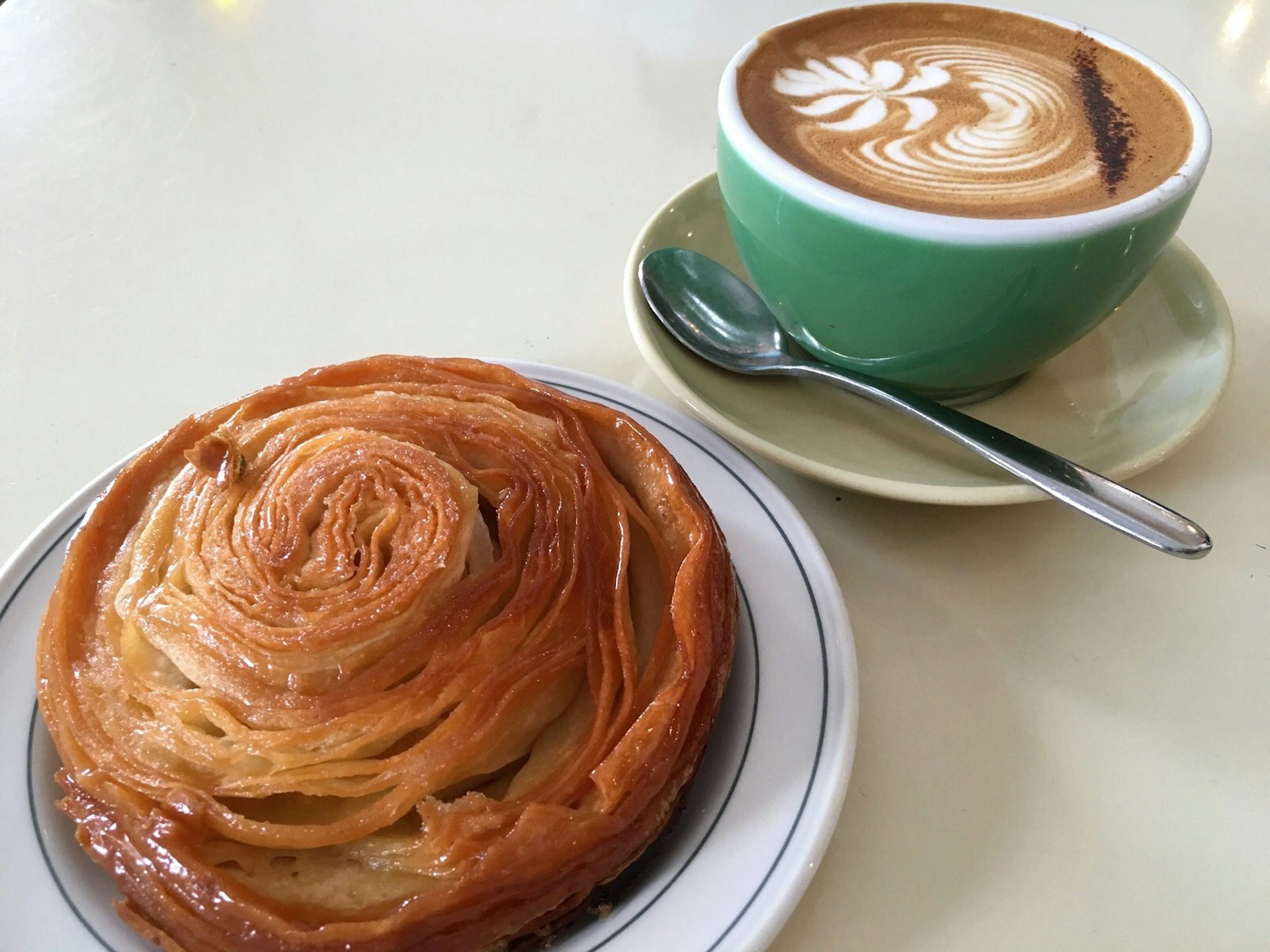 Close up view of a pastry scroll on a plate beside a cup of coffee © Ria de Jong / Lonely Planet