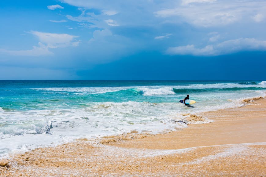 A surfer holding a surfboard runs from the surf to the beach in Bali 
