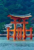 A row boat with 16 rowers approaching a Japanese torii gate, which stands in water; best things to do in the summer in Japan