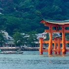 A row boat with 16 rowers approaching a Japanese torii gate, which stands in water; best things to do in the summer in Japan