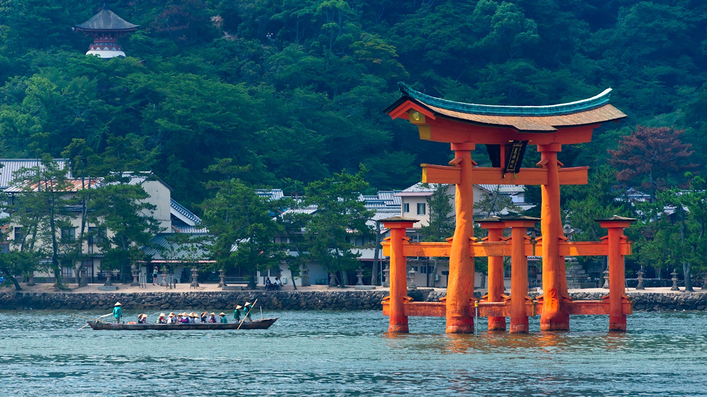A row boat with 16 rowers approaching a Japanese torii gate, which stands in water; best things to do in the summer in Japan