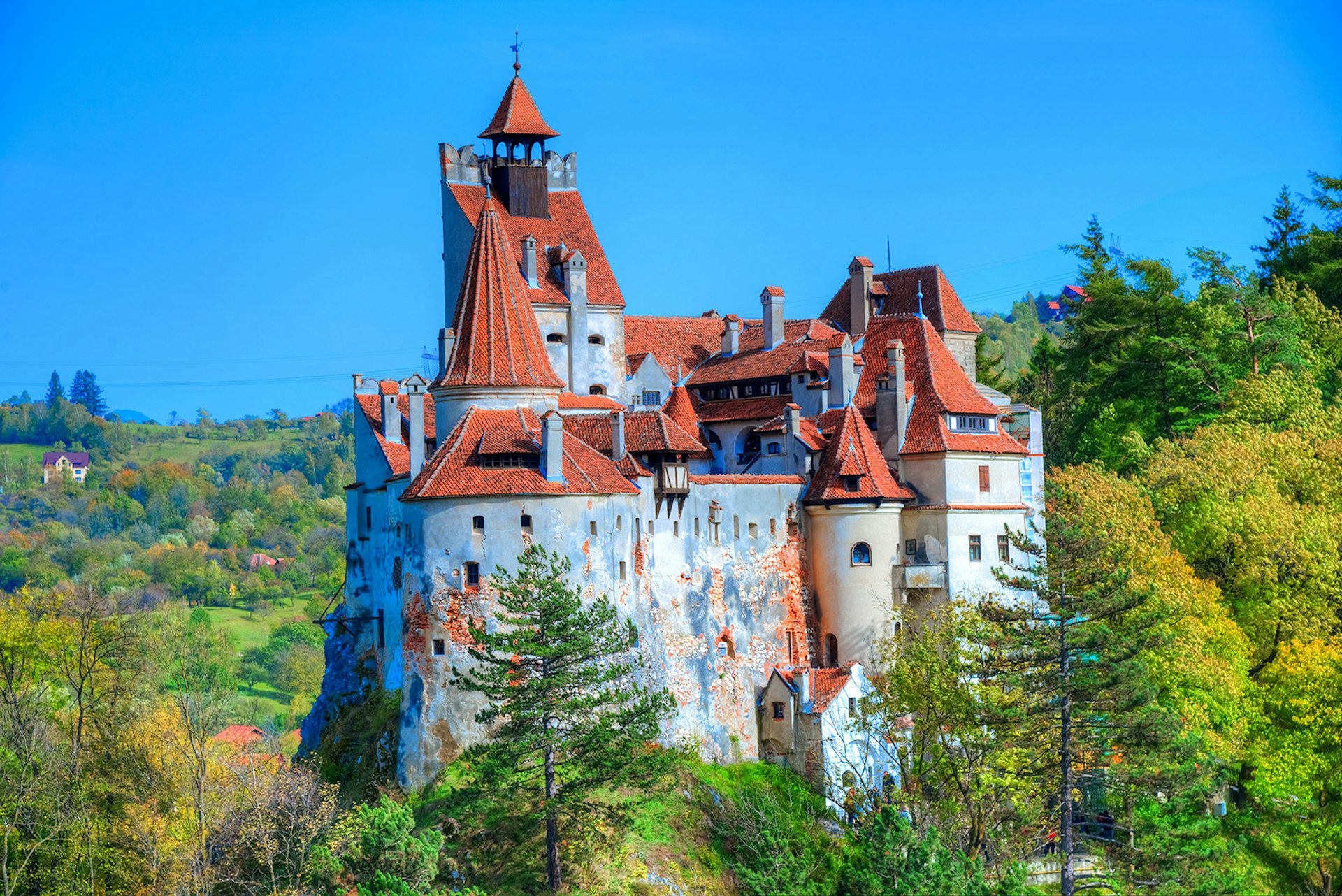 Bran Castle, with its white stone walls and orange roof, stands in the middle of the forest in Transylvania, Romania
