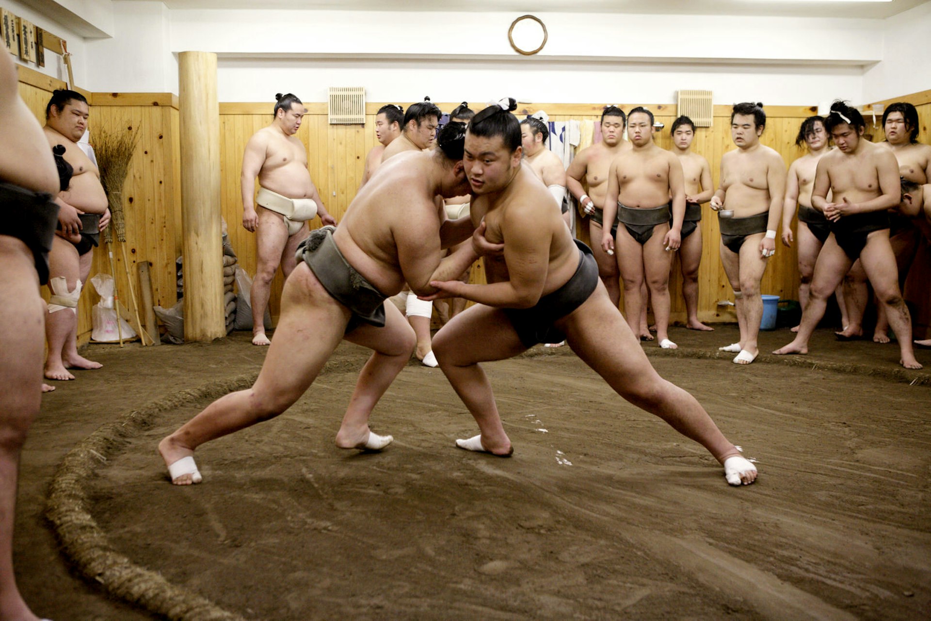 Young sumo wrestlers practice while other wrestlers look on in Tokyo