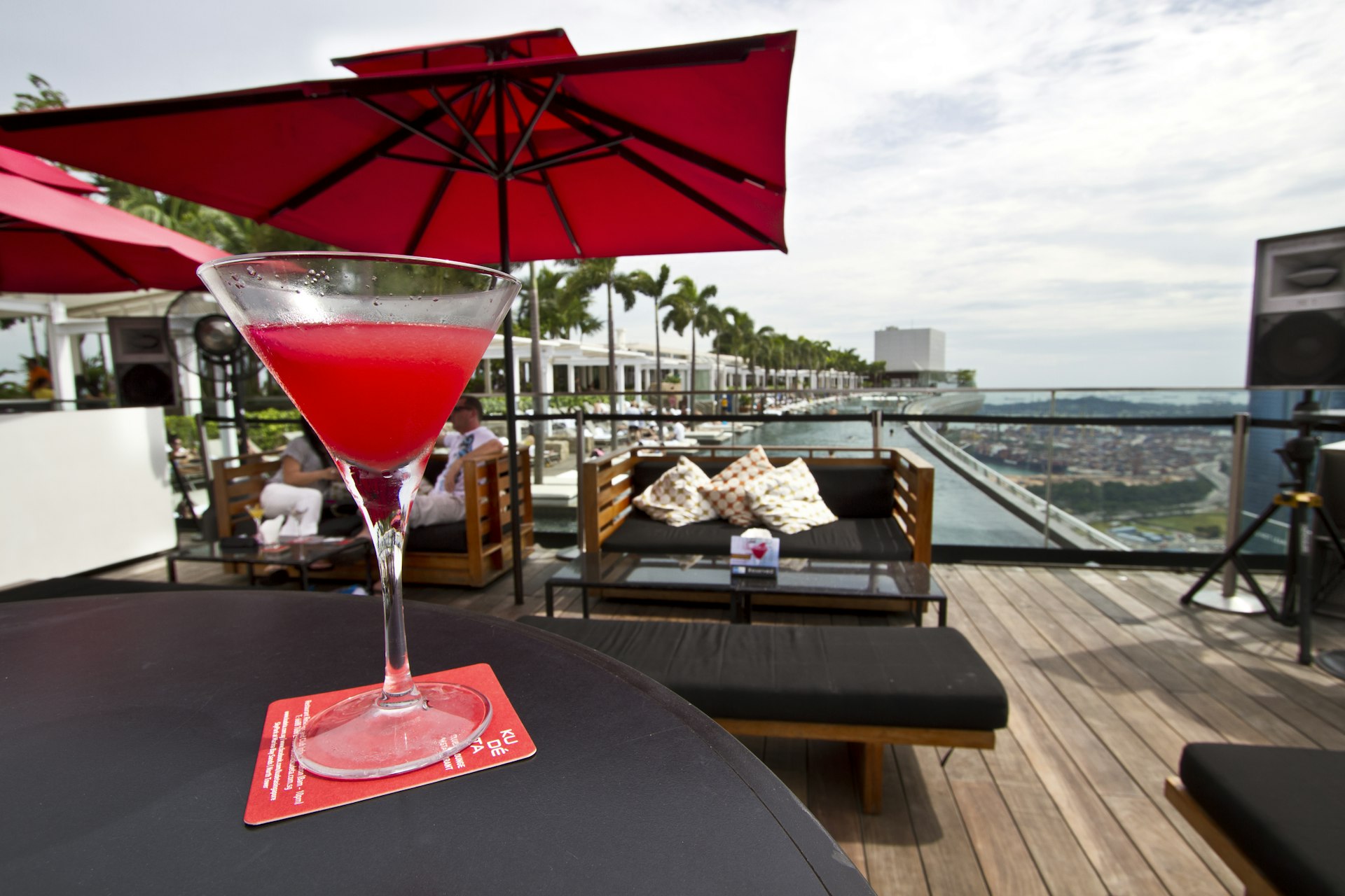 A cocktail glass on a table with a view of a decked rooftop, pool and city in the distance © Kylie McLaughlin / Getty Images