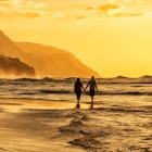 A couple walks along the beach on Kaua‘i. Image by Justin Horrocks / Getty