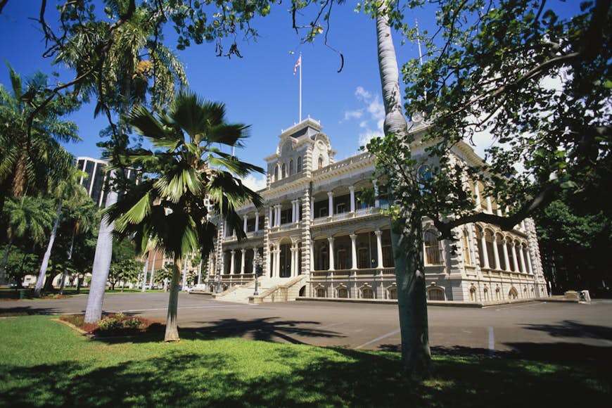 The 'Iolani Palace is seen in its park, surrounded by palm trees under a brilliant blue Hawaii sun. It's the site of lots of Hawaiian and US history.