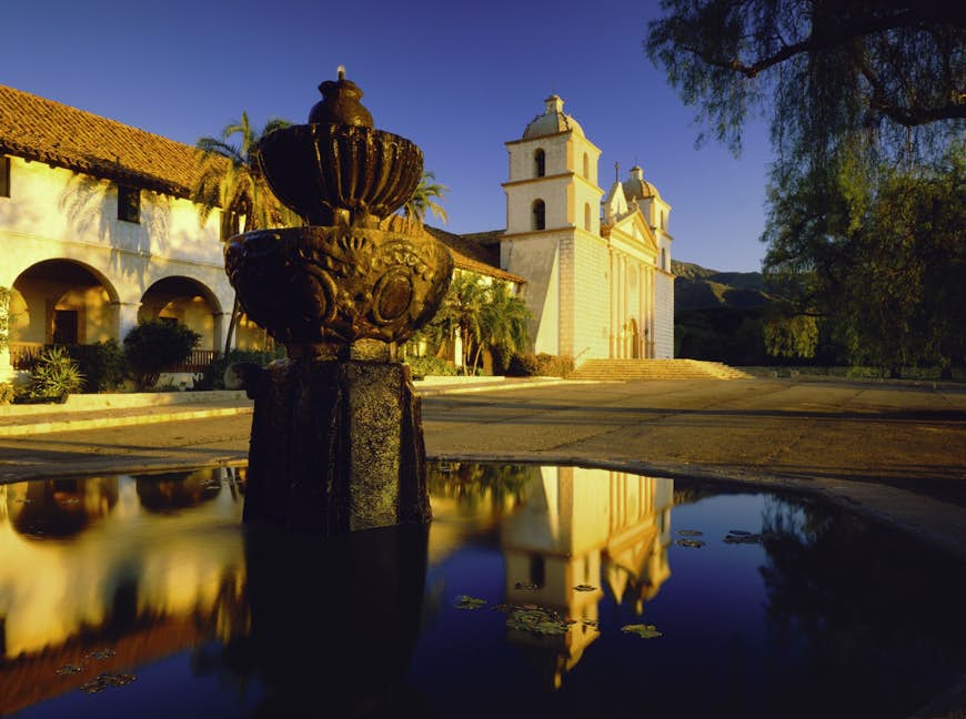 A fountain in the foreground reflects a view of the Santa Barbara Mission of California, a spanish-style church