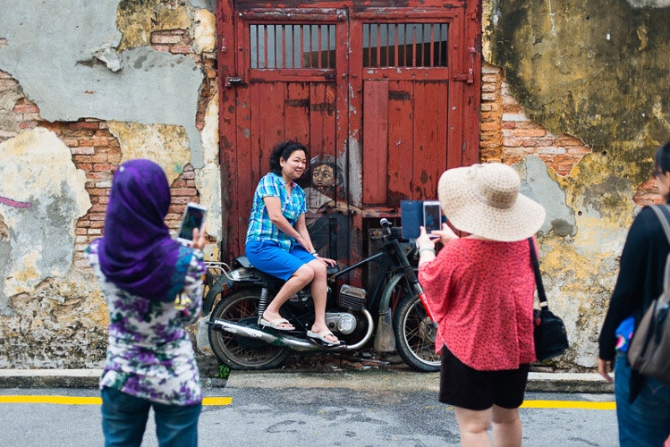 Tourists photographing Old Motorcycle, one of several works by street artist Ernest Zacharevic that has made George Town, Penang, synonymous with street art. Image by Lonely Planet