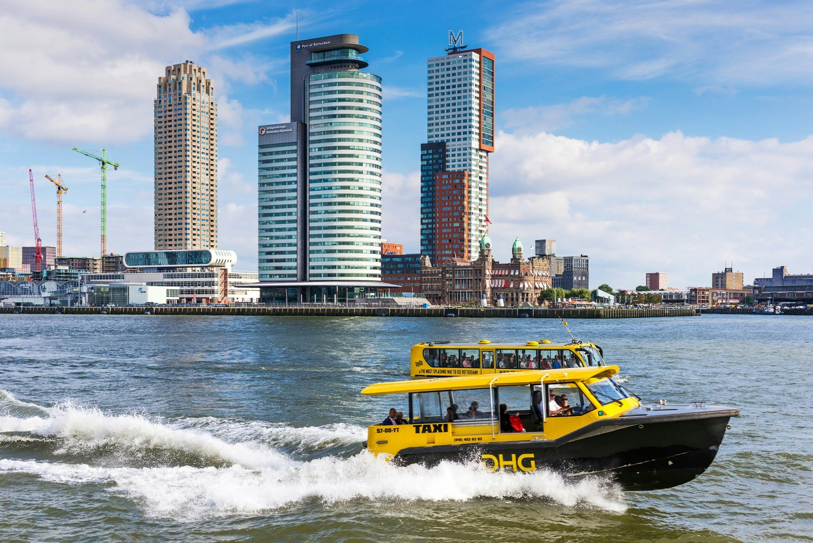 A water taxi and Splash Tours bus on the Nieuwe Maas canal in Rotterdam with Wilhelminapier spit in the background
