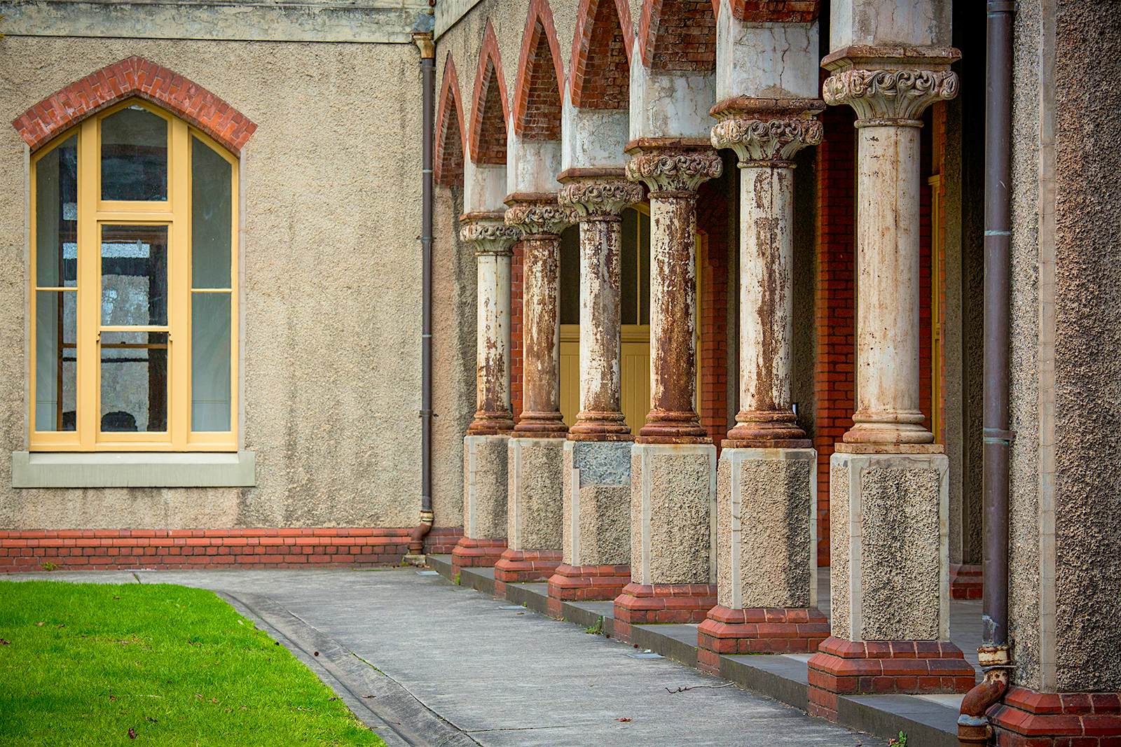 Abbotsford Convent, Melbourne Des piliers en pierre usés bordent une petite pelouse, avec le mur du couvent et une fenêtre cintrée en arrière-plan. Melbourne, Australie.