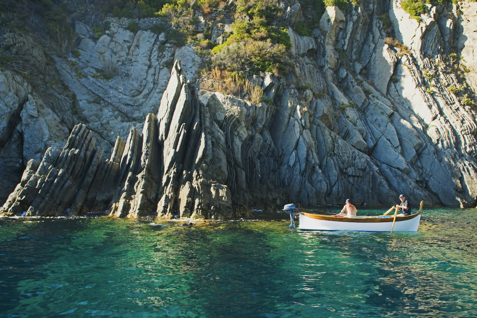 Two people sit in a small motorized canoe against a backdrop of craggy cliffs near the Cinque Terre, Italy