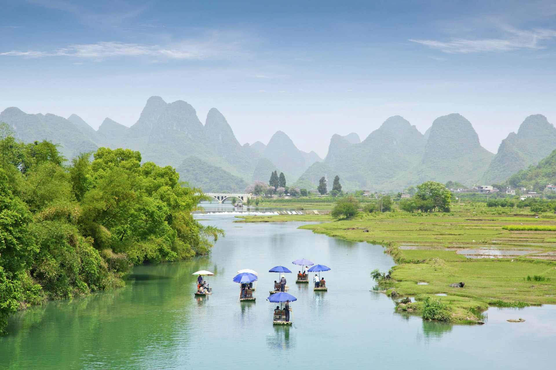 A collection of small boats glide across the river near Guilin. In the distance you can see a range of grass-covered mountains