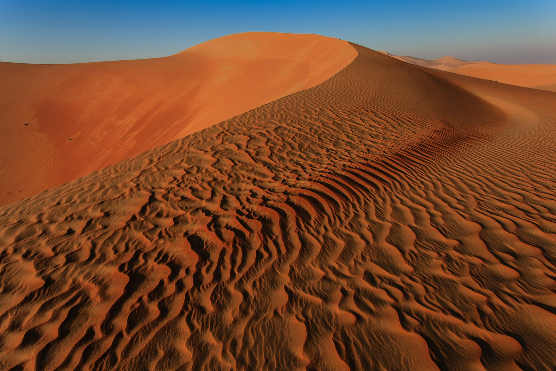 Ripples of sand lead towards the top of a rust-colored dune in the Empty Quarter