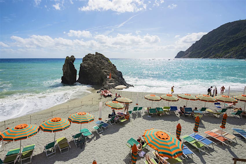 The sandy beach at Monterosso, Cinque Terre, lined with pink and green striped umbrellas and beach loungers