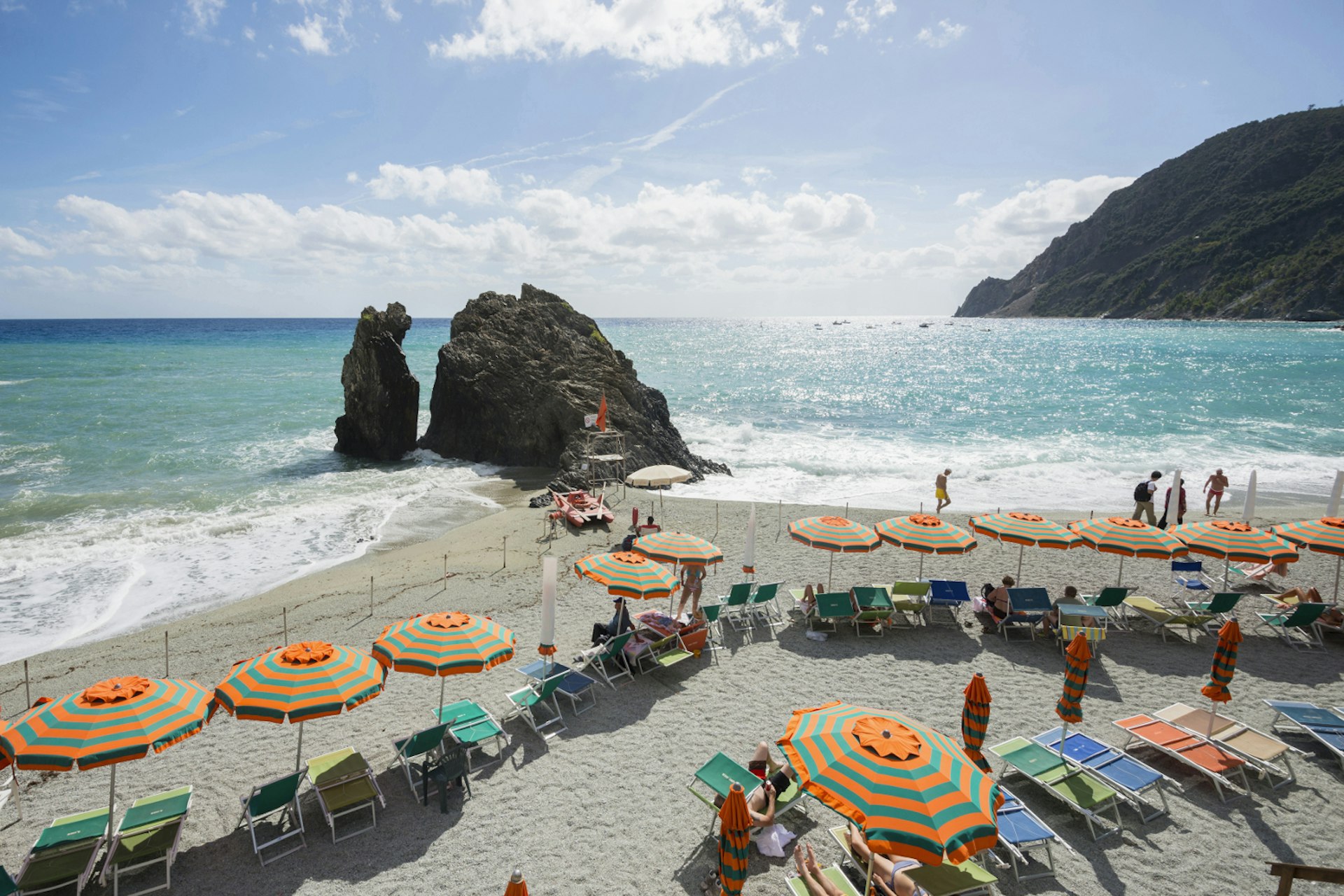 The sandy beach at Monterosso, Cinque Terre, lined with pink and green striped umbrellas and beach loungers