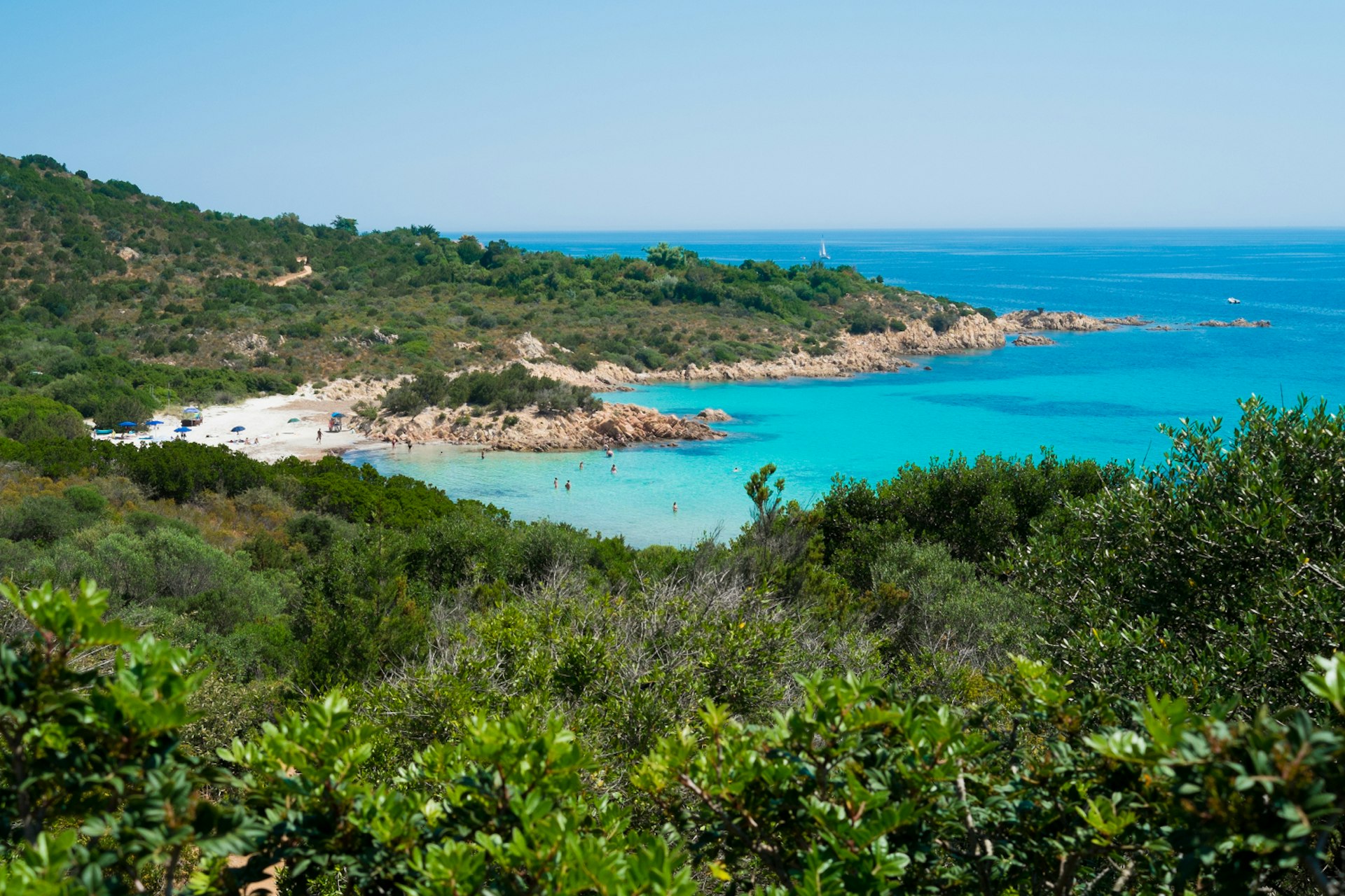 Landscape shot of Spiaggia del Principe with greenery backing the white-sand beach and light blue waters.