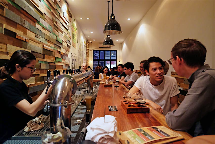 Features - Pasteur_Street_HCMC-4e1863d4434c Patrons sit and drink at a long narrow bar while a server pours a beer at Pasteur Street Brewing Company