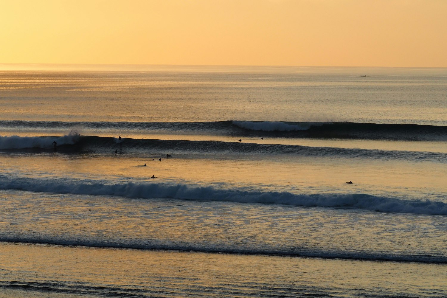 Surfers catch their last waves of the day as the sun sets over the horizon at Bingin, Bali