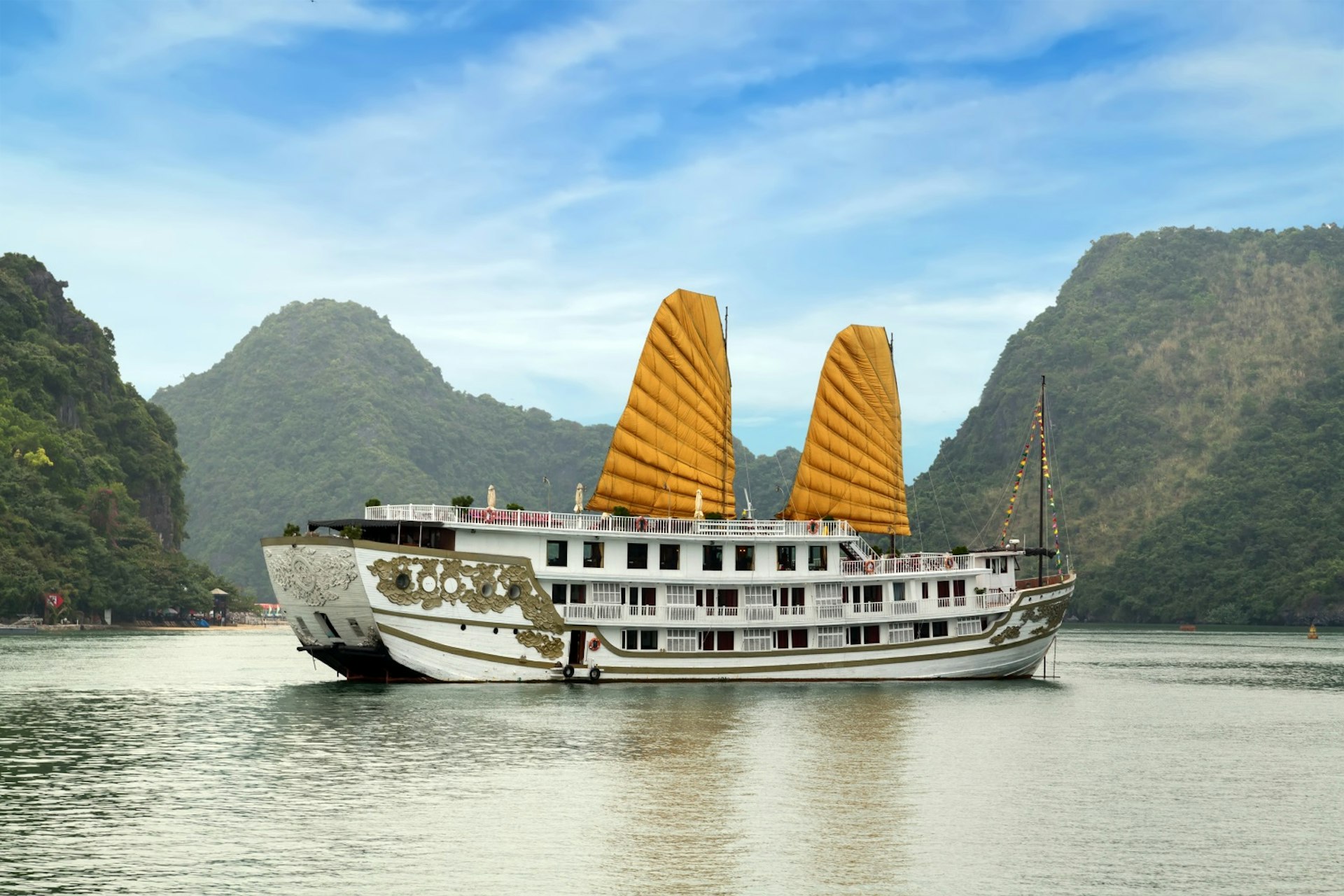 A cruise ship outfitted with a pair of large yellow sails glides along in Halong Bay 
