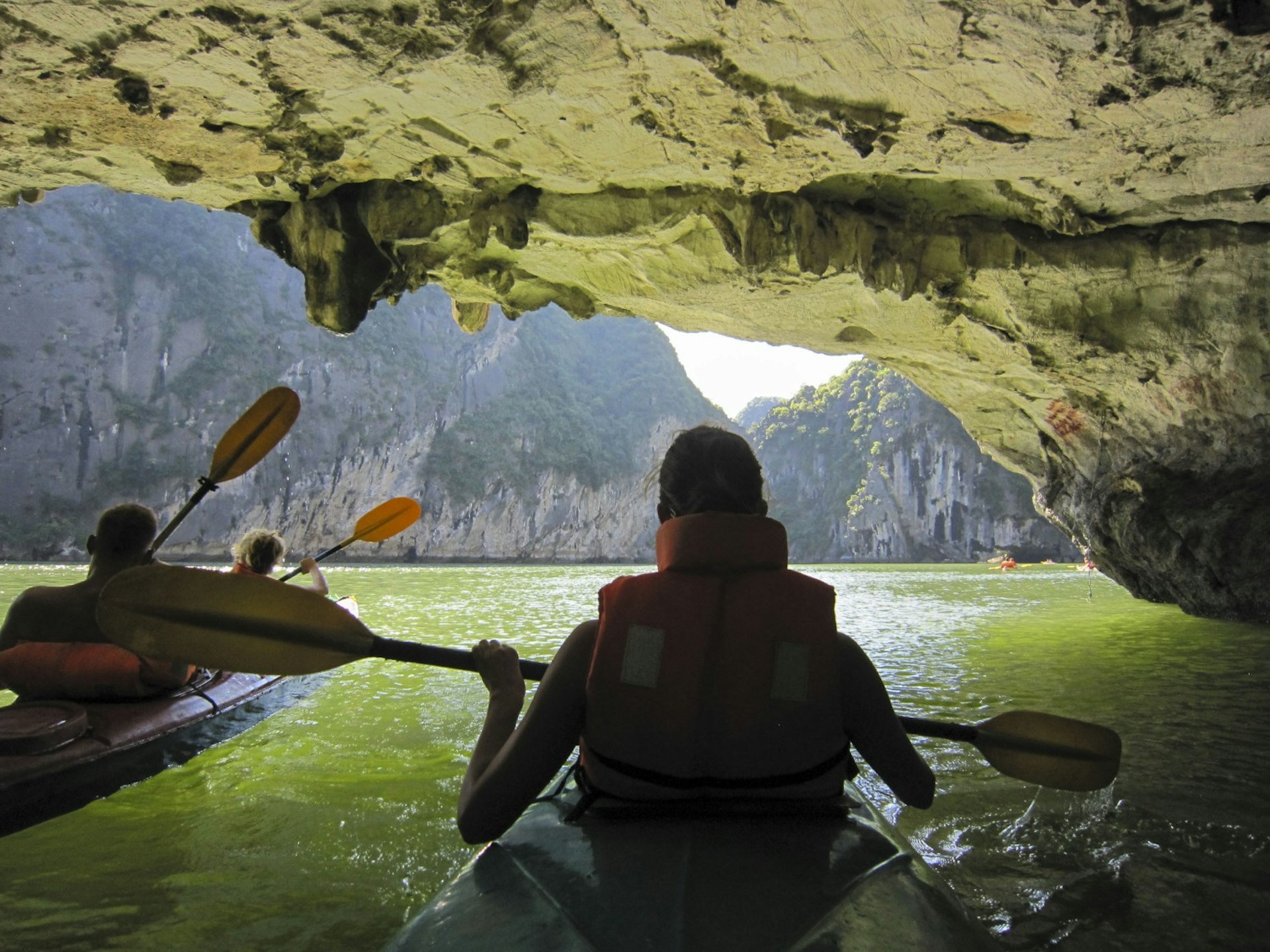 A group of kayakers (equipped with life jackets and paddles) make their way through a dimly lite cave in Halong Bay