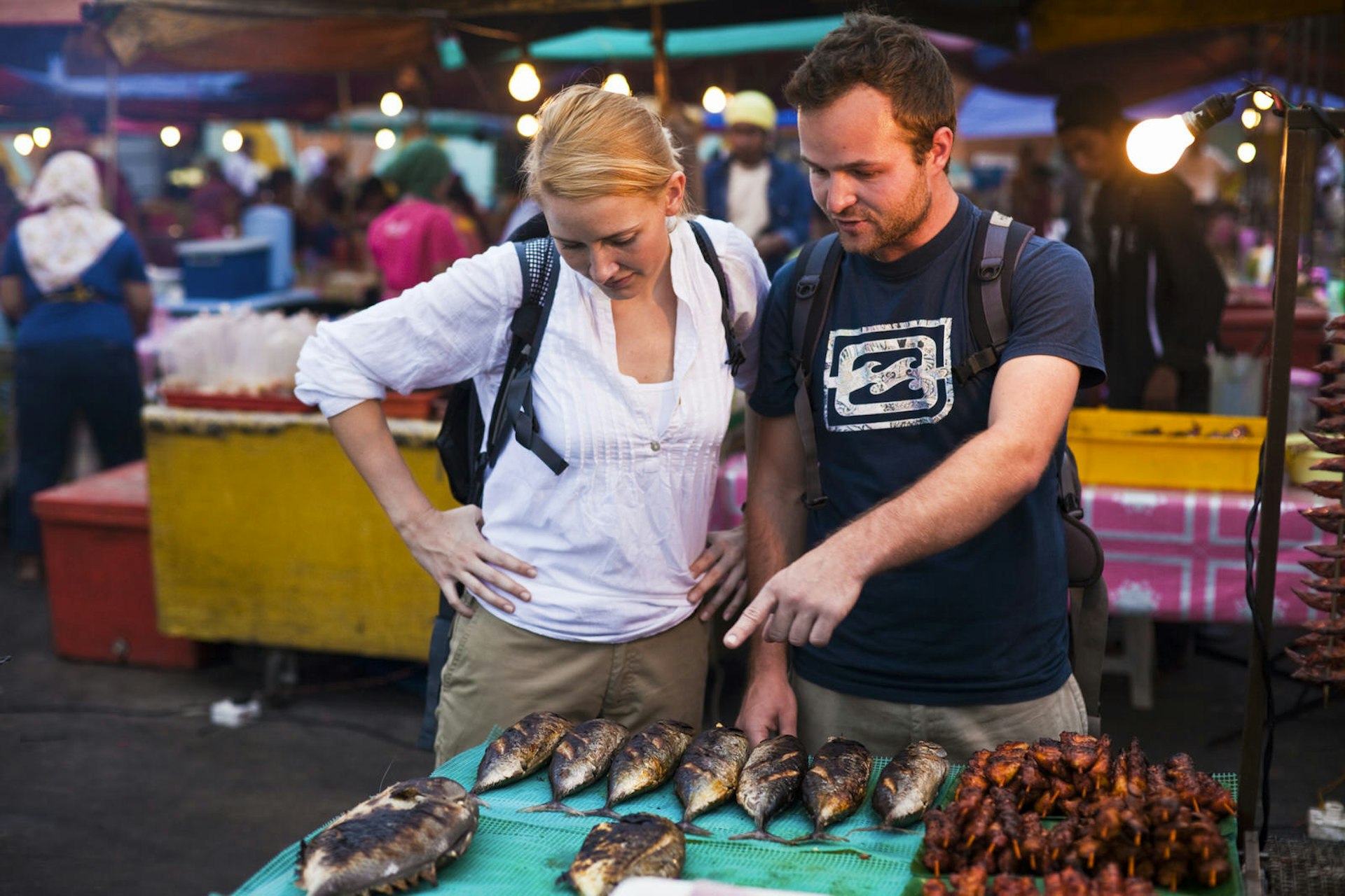 A couple inspecting some fresh fish in a street food market