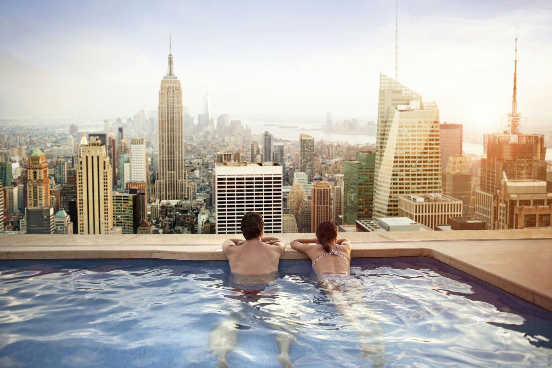 A couple in a rooftop pool staring out at the Manhattan skyline