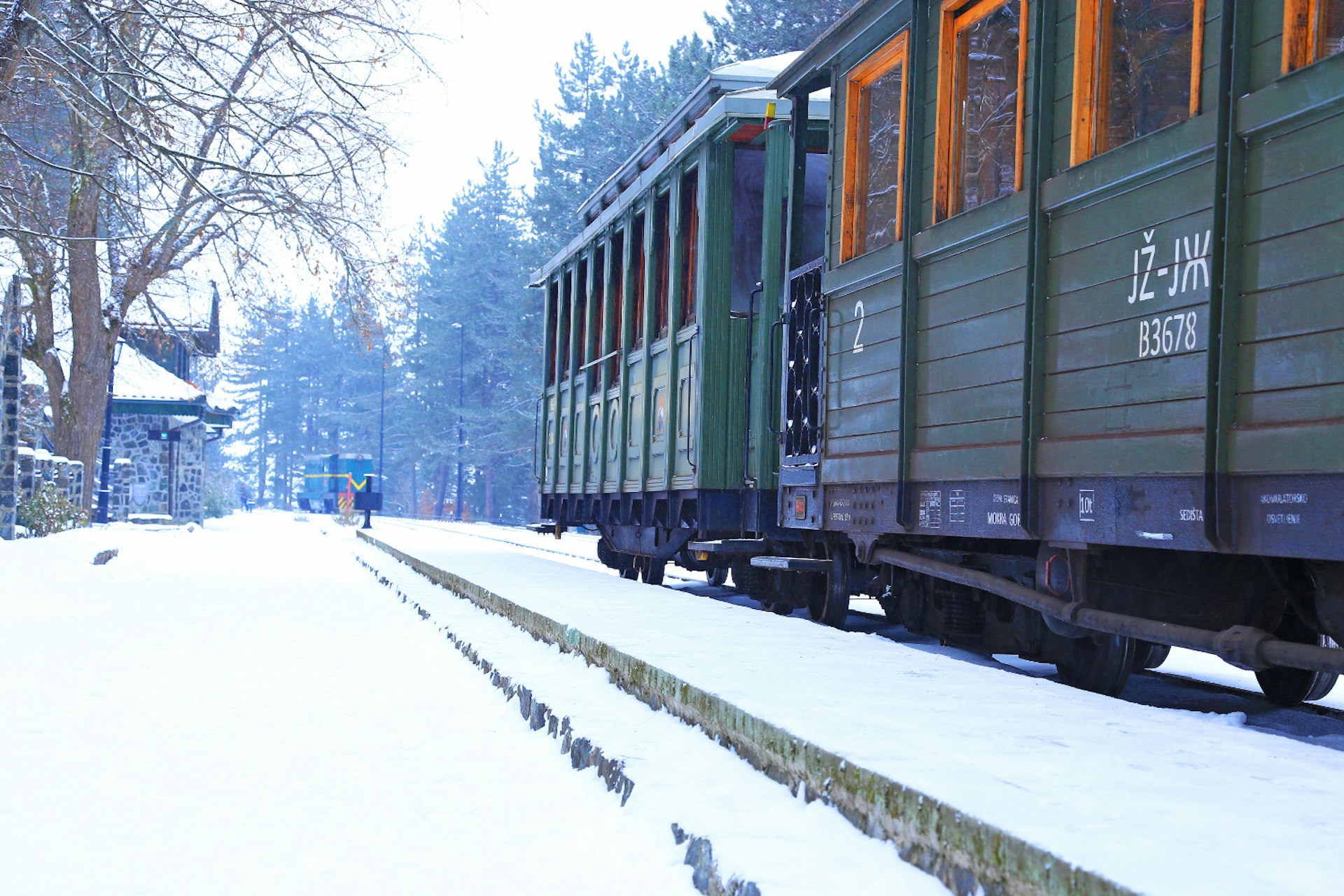 Two dark green wooden carriages of the Šargan Eight narrow-gauge heritage railway stand in the snow