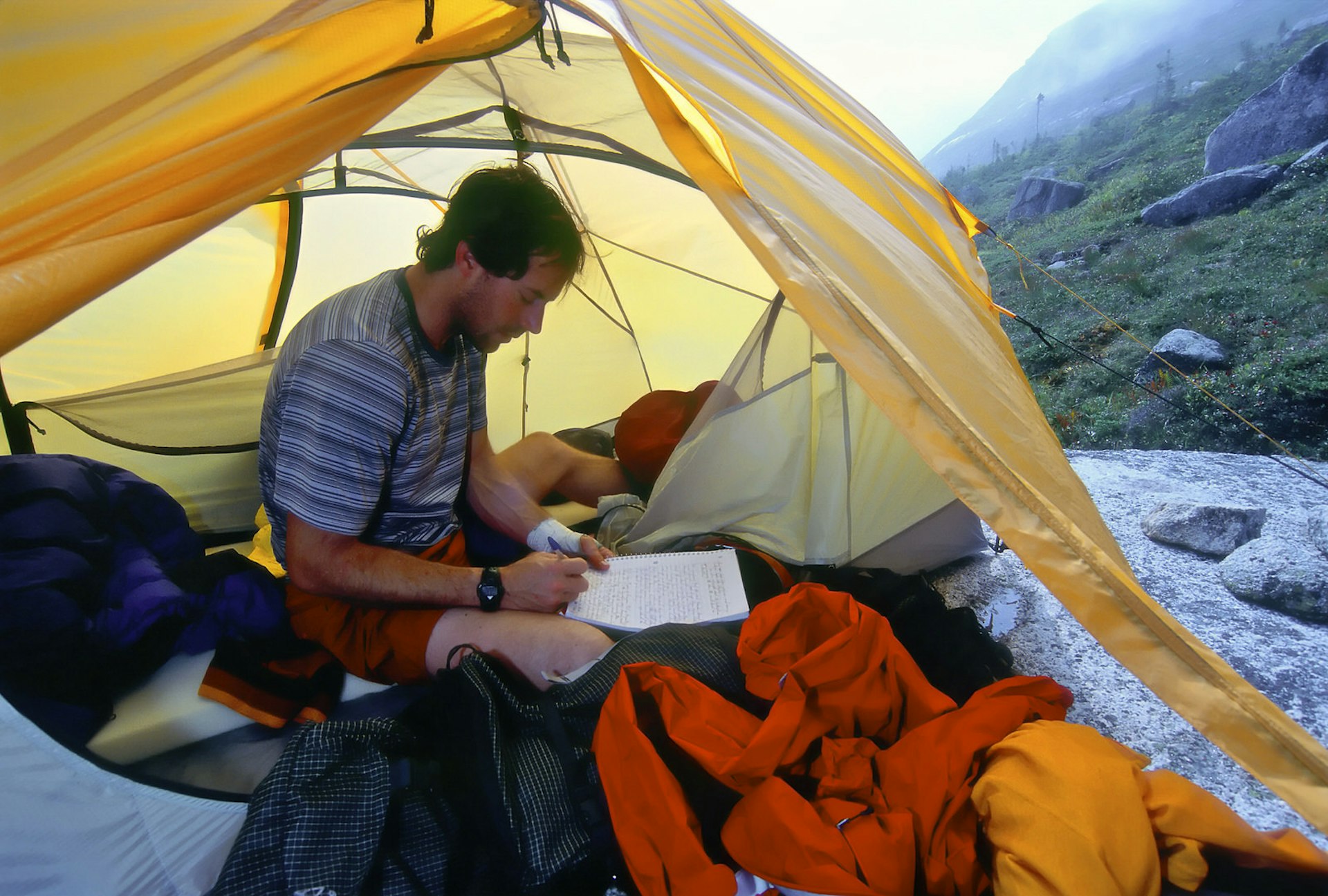 A man writing in a journal in a tent