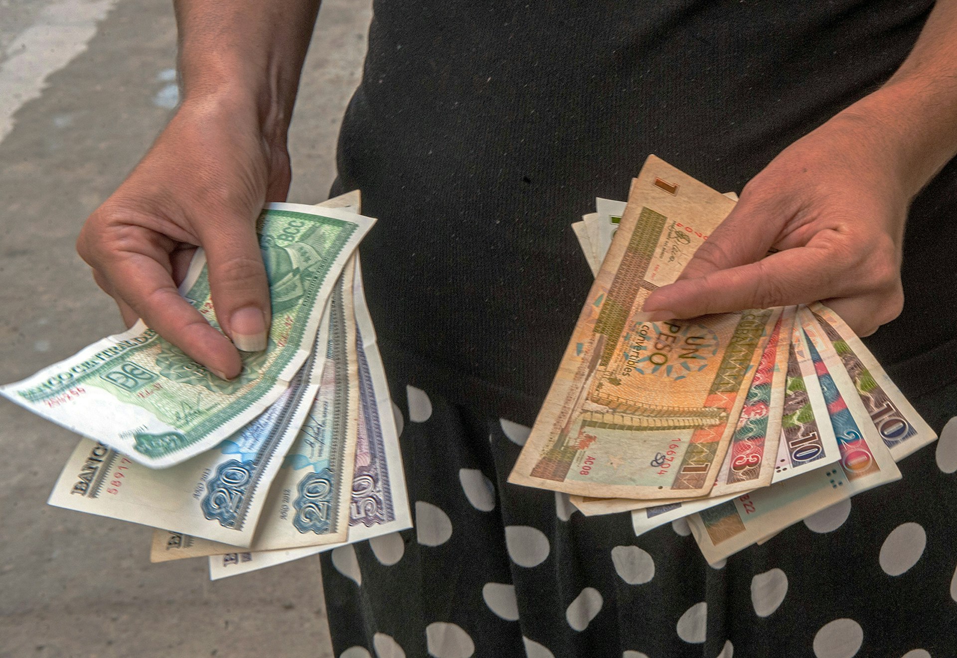 A Cuban shows Cuban Pesos CUP (Left hand) and Convertible Pesos CUC (Right hand), © Yamil Lage / Getty Images