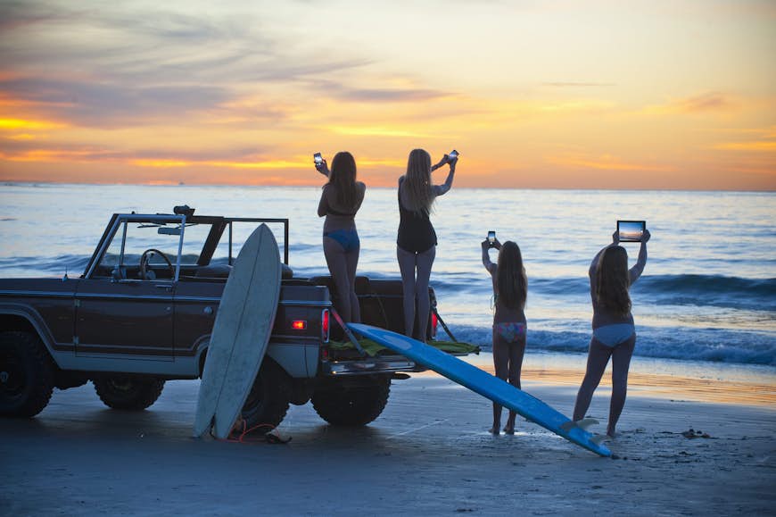 solnedgång på stranden, flickor med smarta telefoner och surfplatta