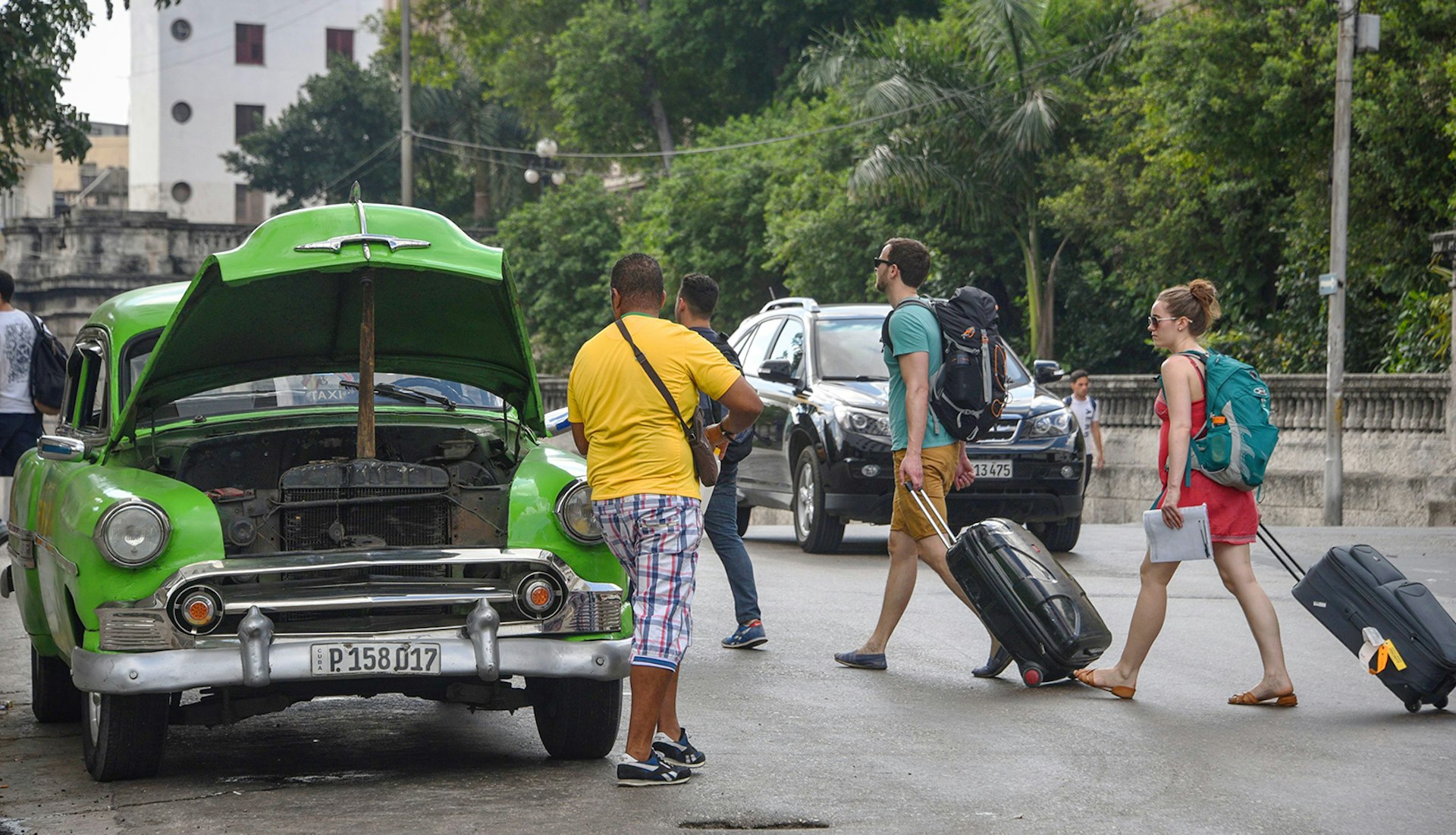 A man repairs his car as tourists walk past in Havana © Rodrigo Arangua / Getty Images