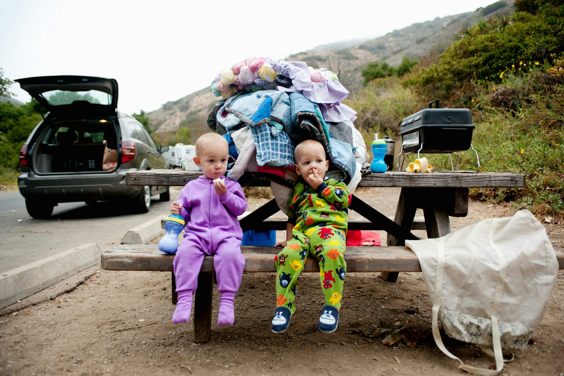 Toddler twins eating banana on picnic bench